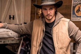 Luke Grimes leans up against a bed.