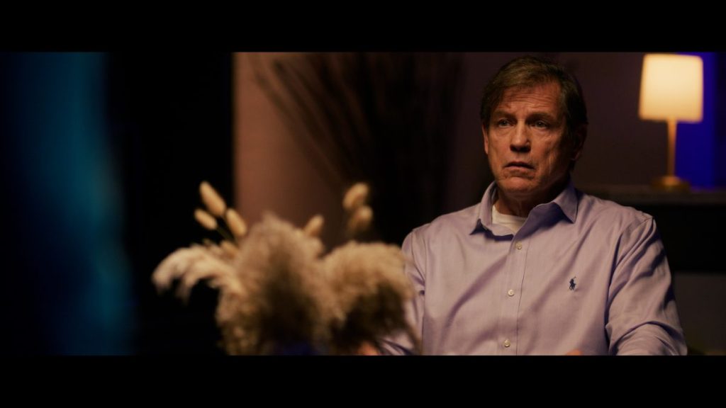 A man sits at a table in Morgan: Killer Doll.