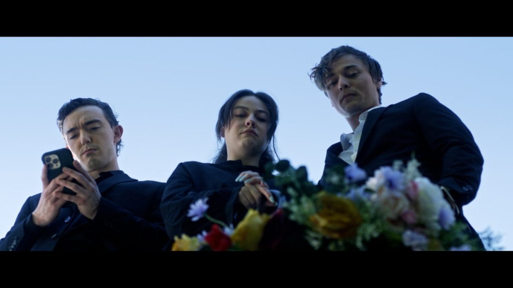 Three people stand at a funeral in Morgan: Killer Doll.